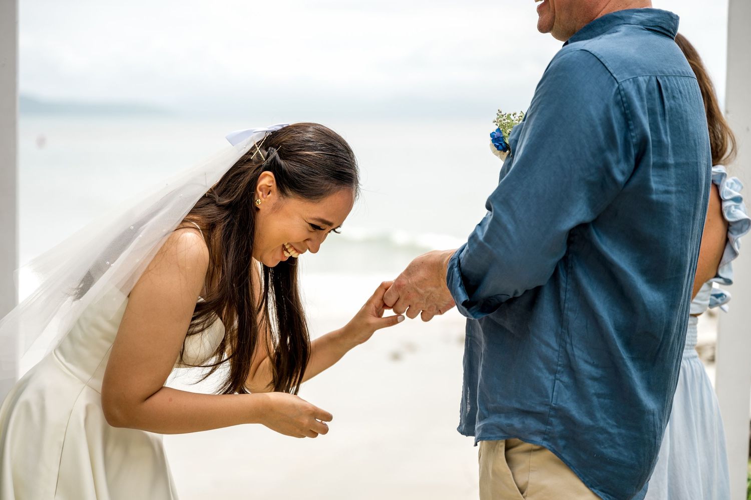 Bride laughing joyfully while placing wedding ring on grooms finger during beach ceremony at Little Cove, Port Douglas.