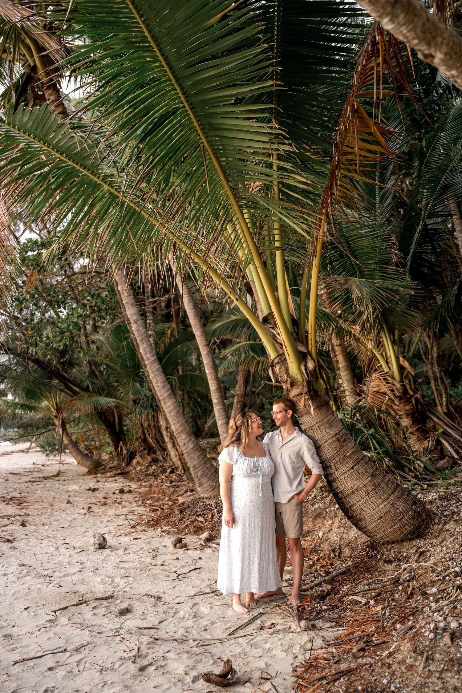 Romantic couple walking hand in hand on sandy beach lined with tall coconut palm trees at Four Mile Beach, Port Douglas.