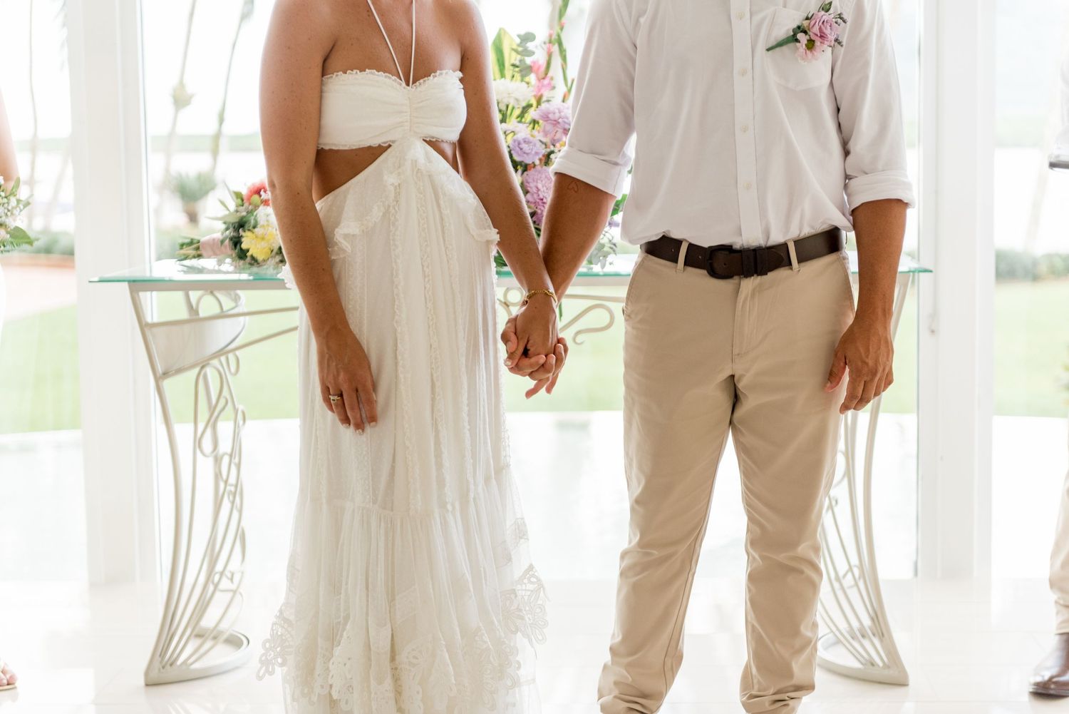 Bride and groom holding hands at altar, bride wearing elegant white halter wedding dress.