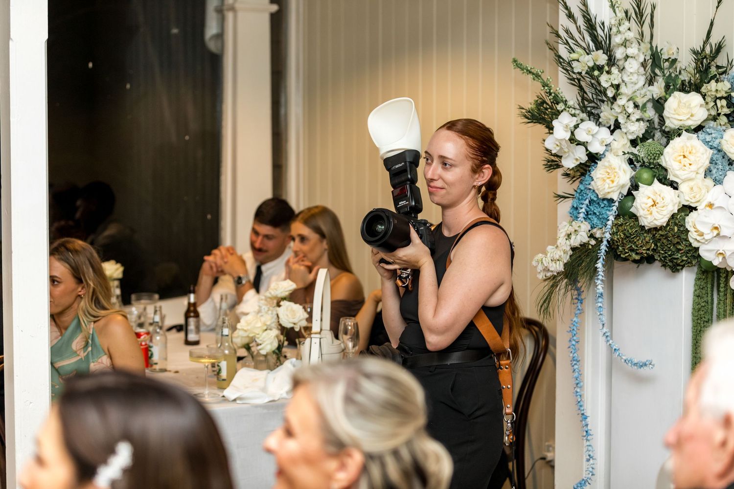 Female photographer with flash capturing moments at elegant wedding reception dinner.