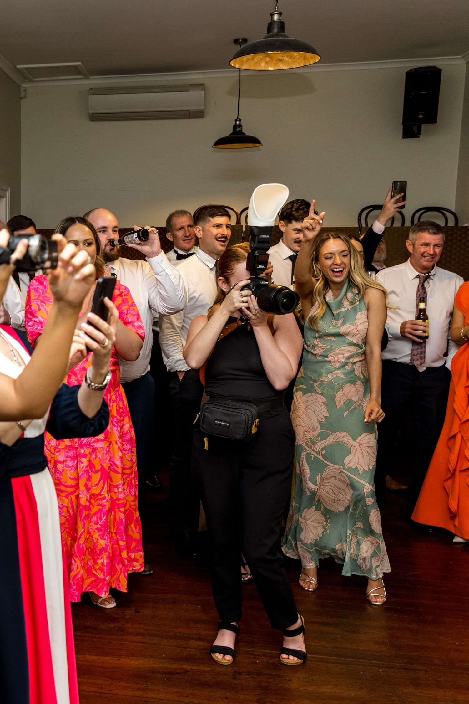 Energetic female photographer with camera enjoying lively wedding reception dance floor.