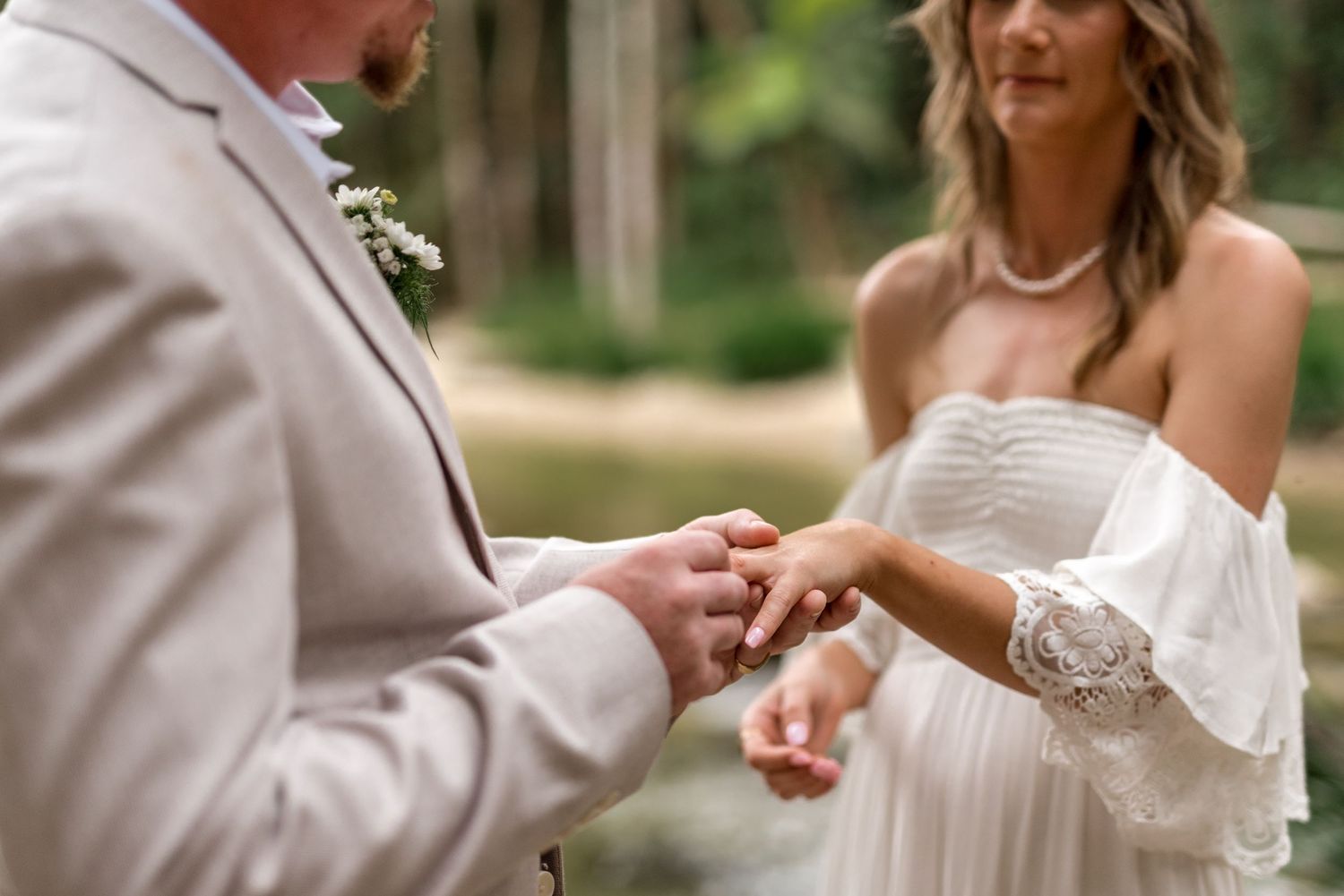 Groom places wedding ring on brides finger during intimate outdoor forest elopement ceremony.