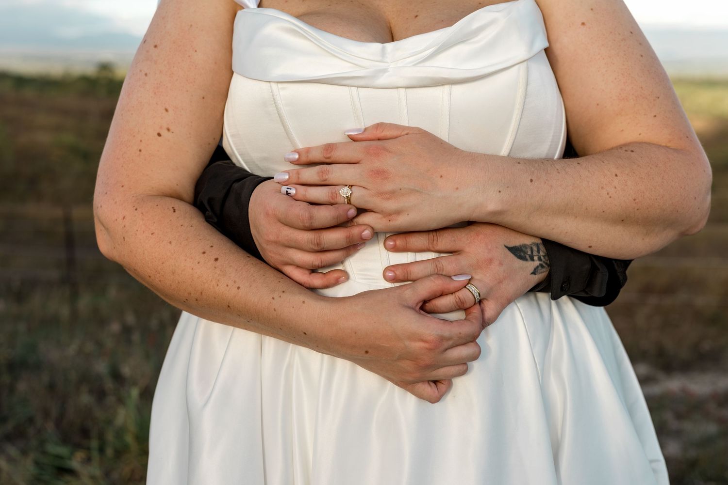 Close-up of bride and groom's hands embracing around bride's white wedding dress.