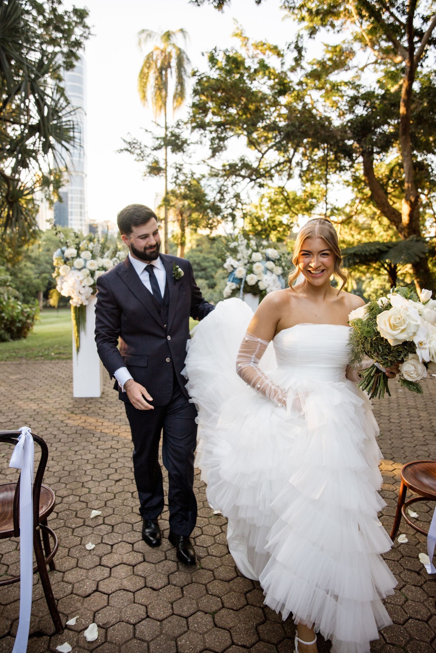 Newlyweds walk back down aisle after outdoor garden wedding ceremony at golden hour.