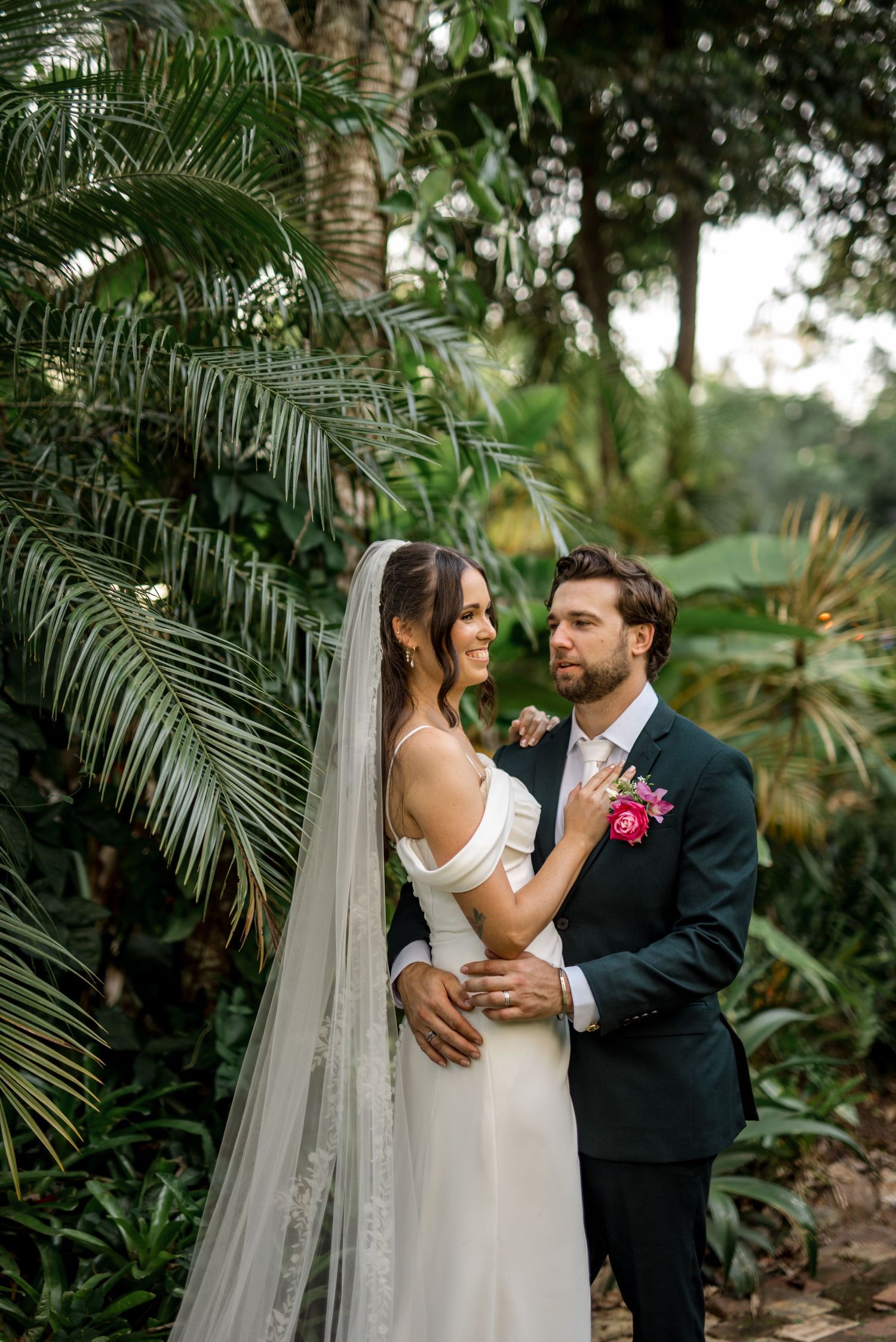 Bride and groom embrace in a lush tropical garden on their wedding day.