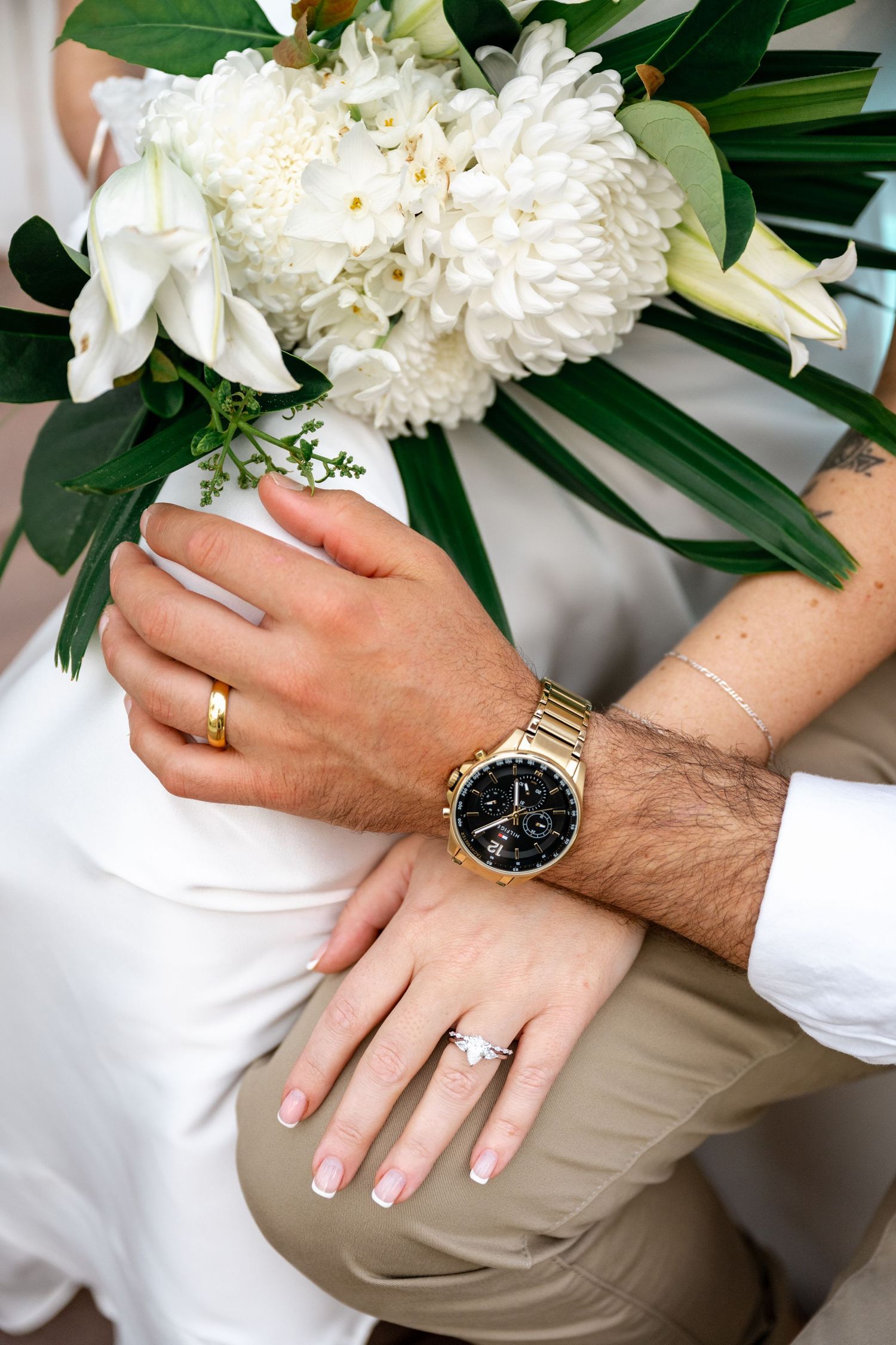 Close-up of bride and groom hands showing wedding rings, gold watch, and a white tropical bouquet at Sheraton Grand Mirage Port Douglas.