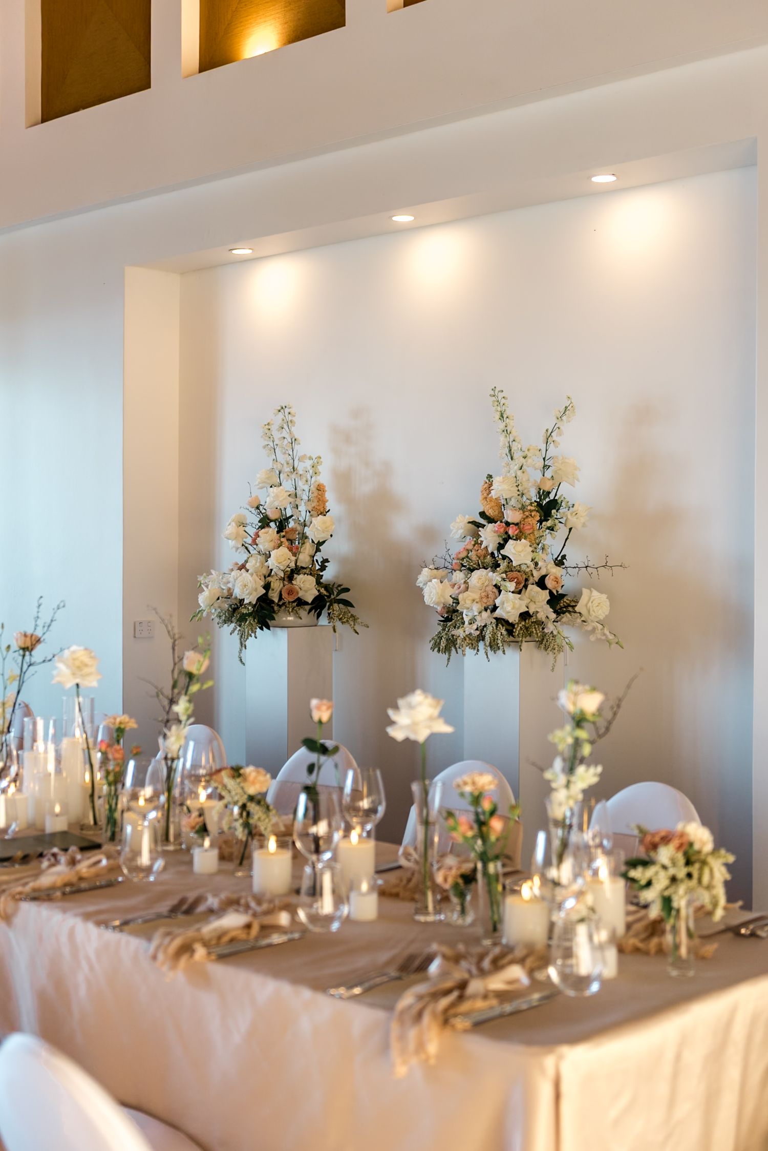 Wedding head table decorated with tall floral arrangements of white and peach roses, candles, and glassware.