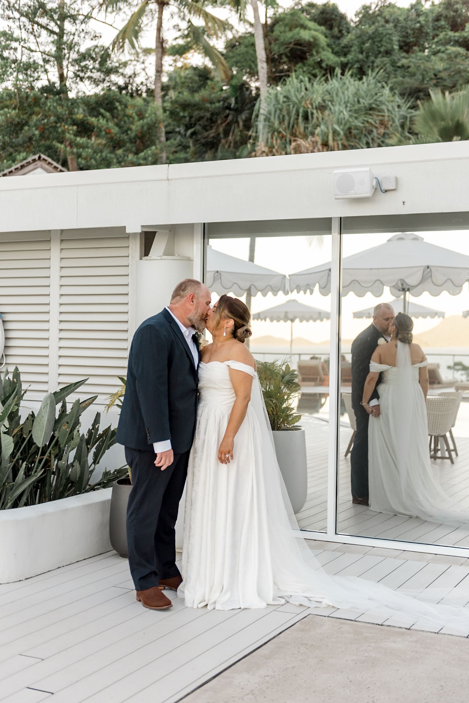 Bride and groom sharing a kiss on a white deck with ocean views at sunset.