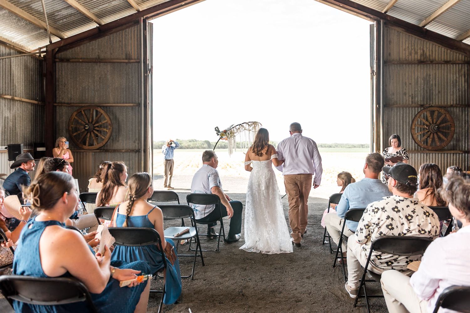 Bride and groom walk down barn aisle with guests seated on either side during ceremony.