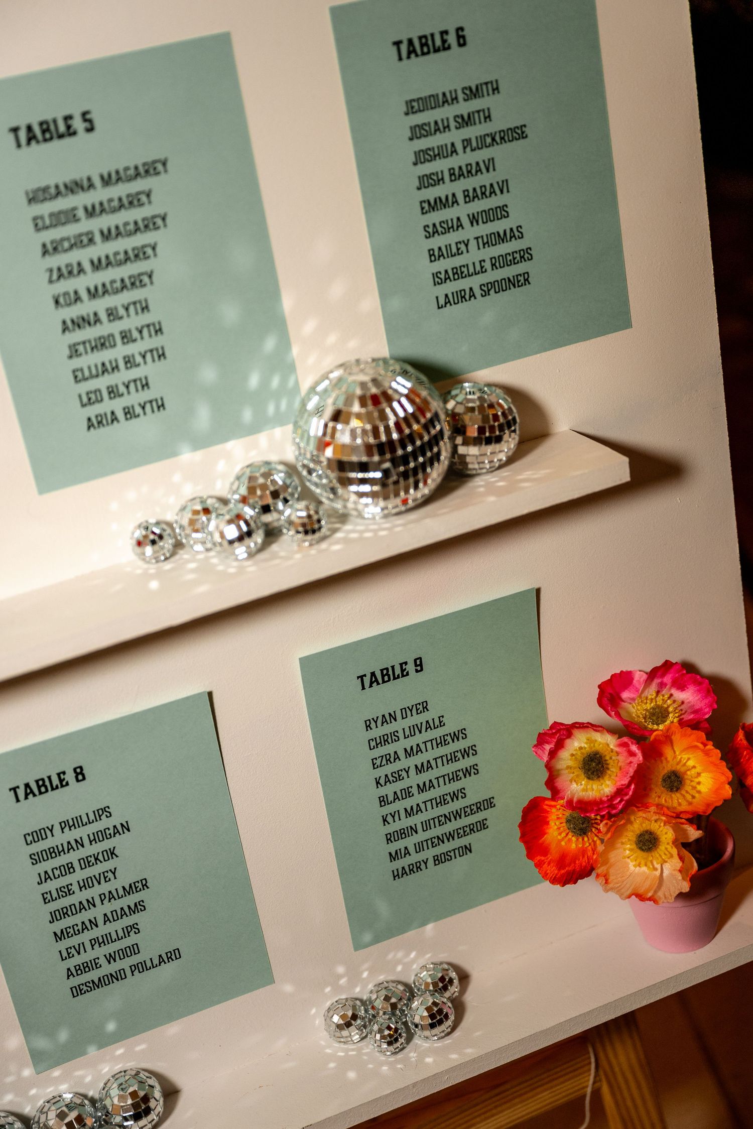 Wedding seating chart display with mint green table cards, silver disco balls, and bright orange and pink floral arrangement.
