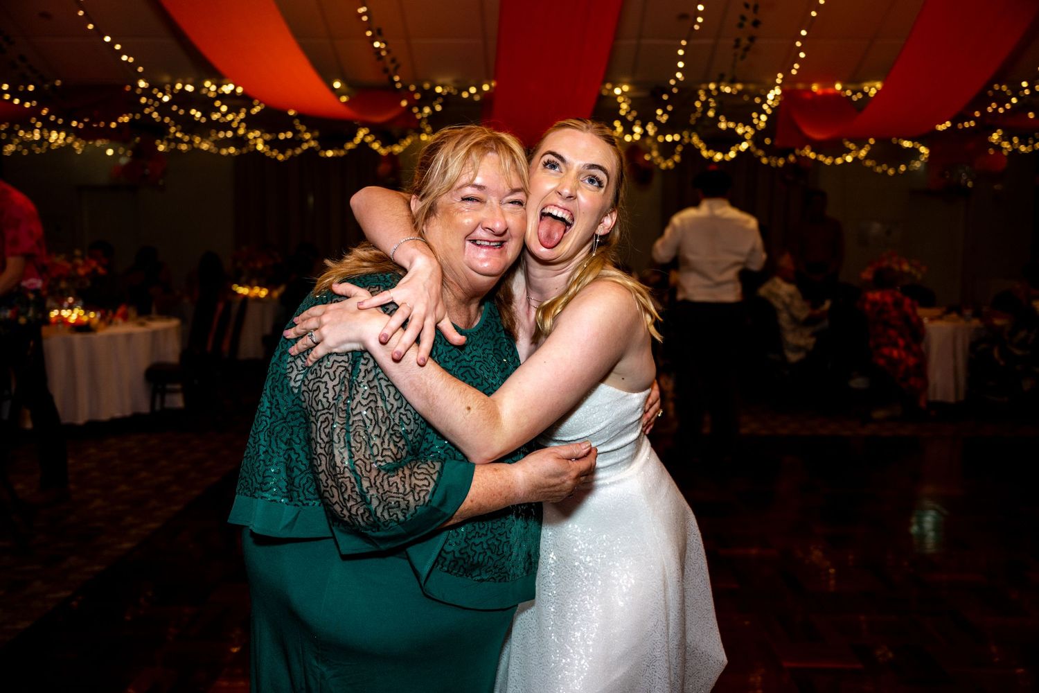 Bride in white dress shares an excited hug with a guest in green.