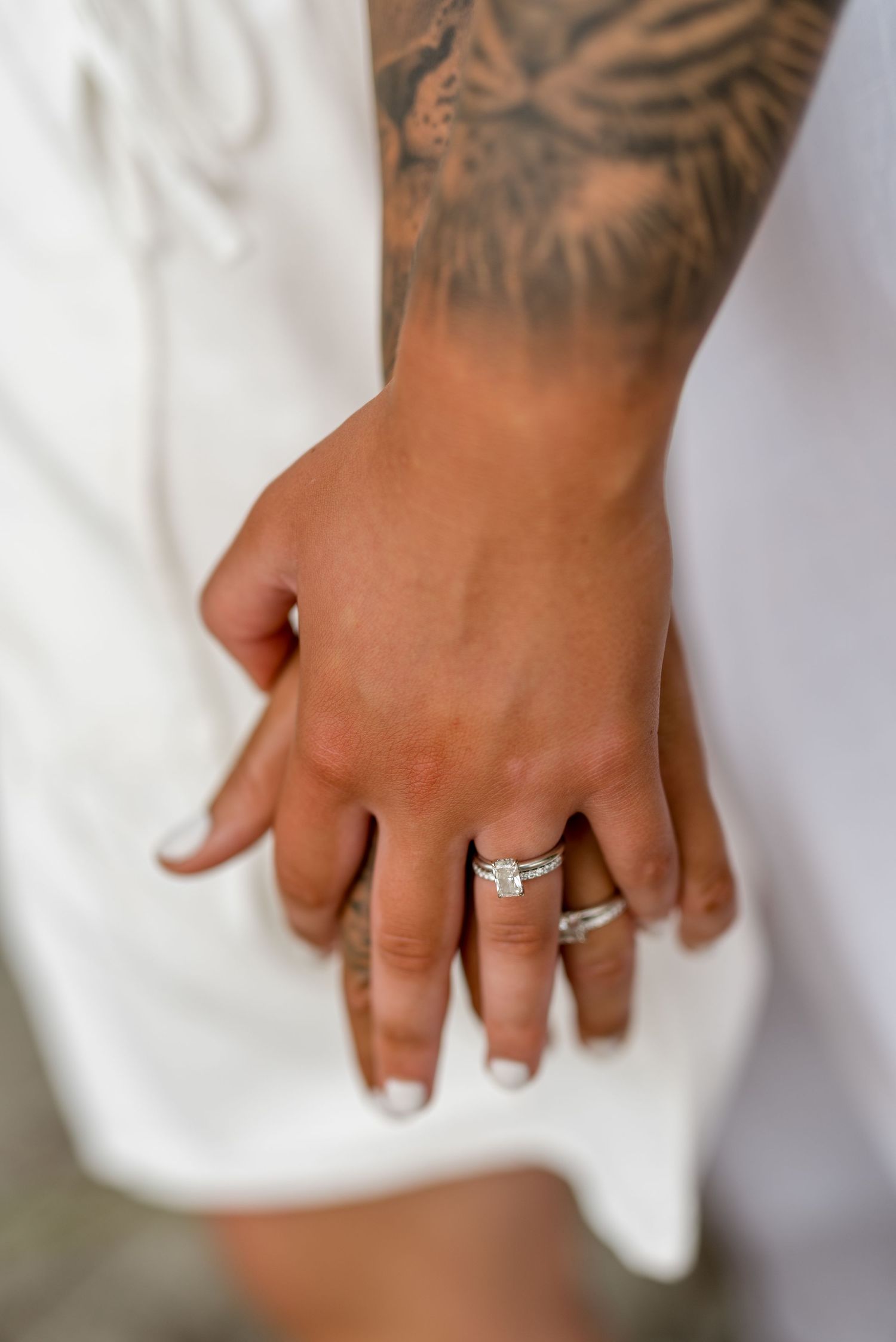 Close-up of two women holding hands showing wedding rings, with a tiger tattoo visible on one arm.