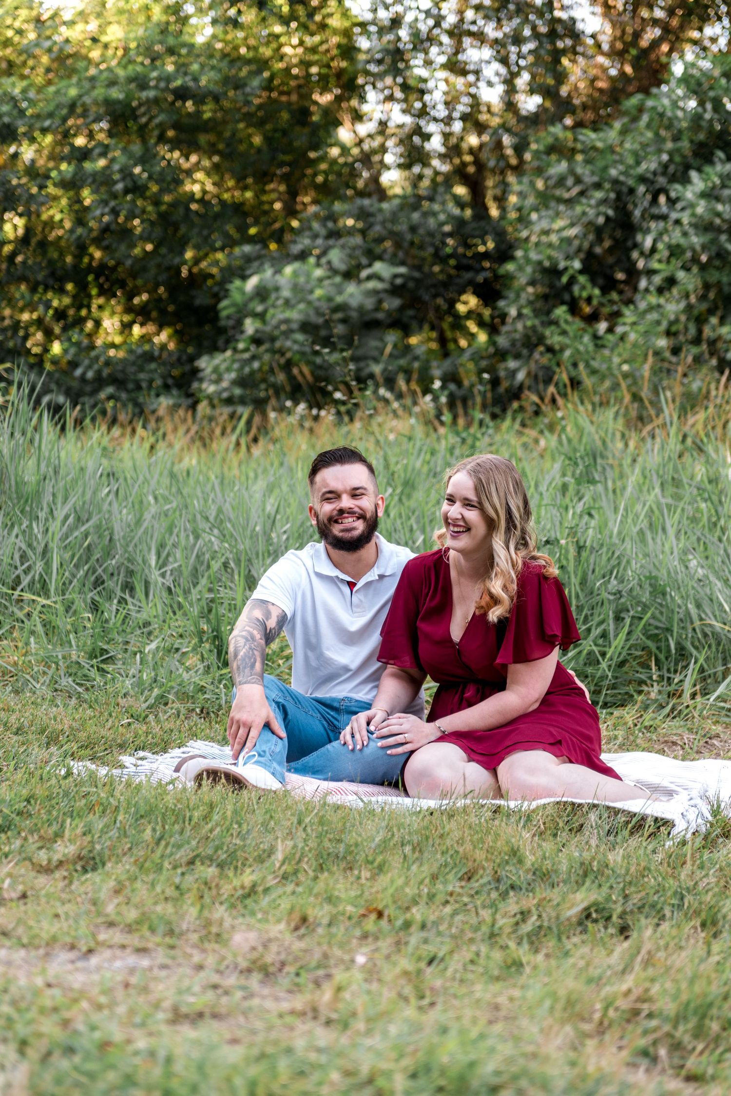 Smiling couple sitting together on a blanket in a grassy meadow enjoying a relaxed outdoor picnic moment.