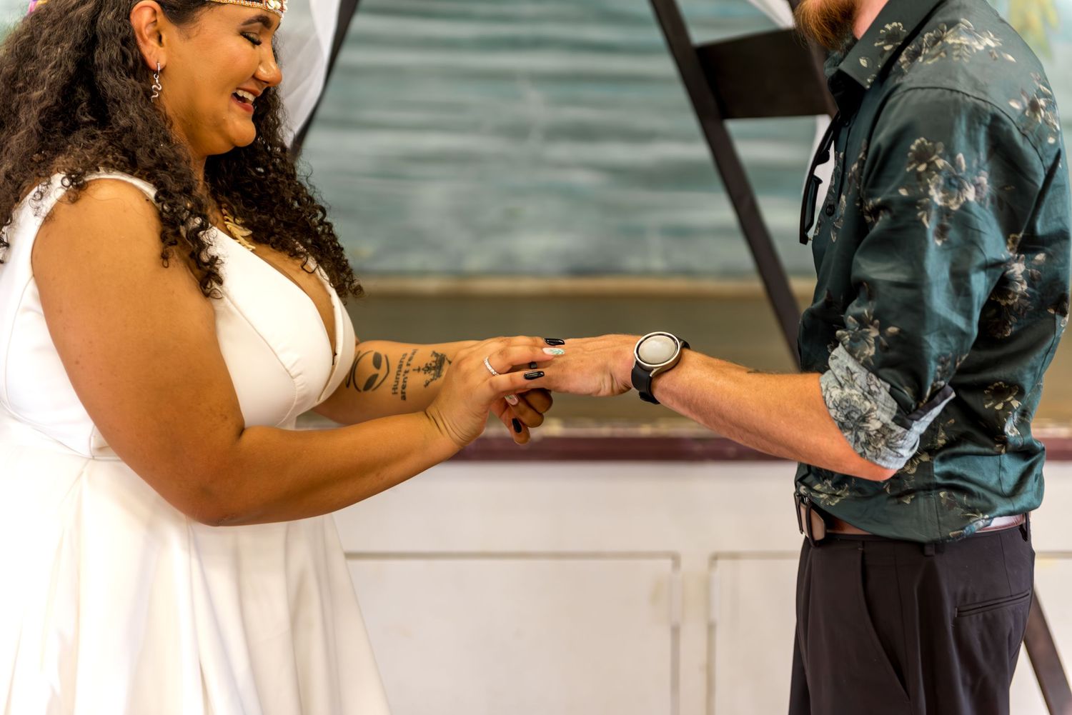 Bride with curly hair and tattoo exchanges rings with groom during intimate wedding ceremony moment.