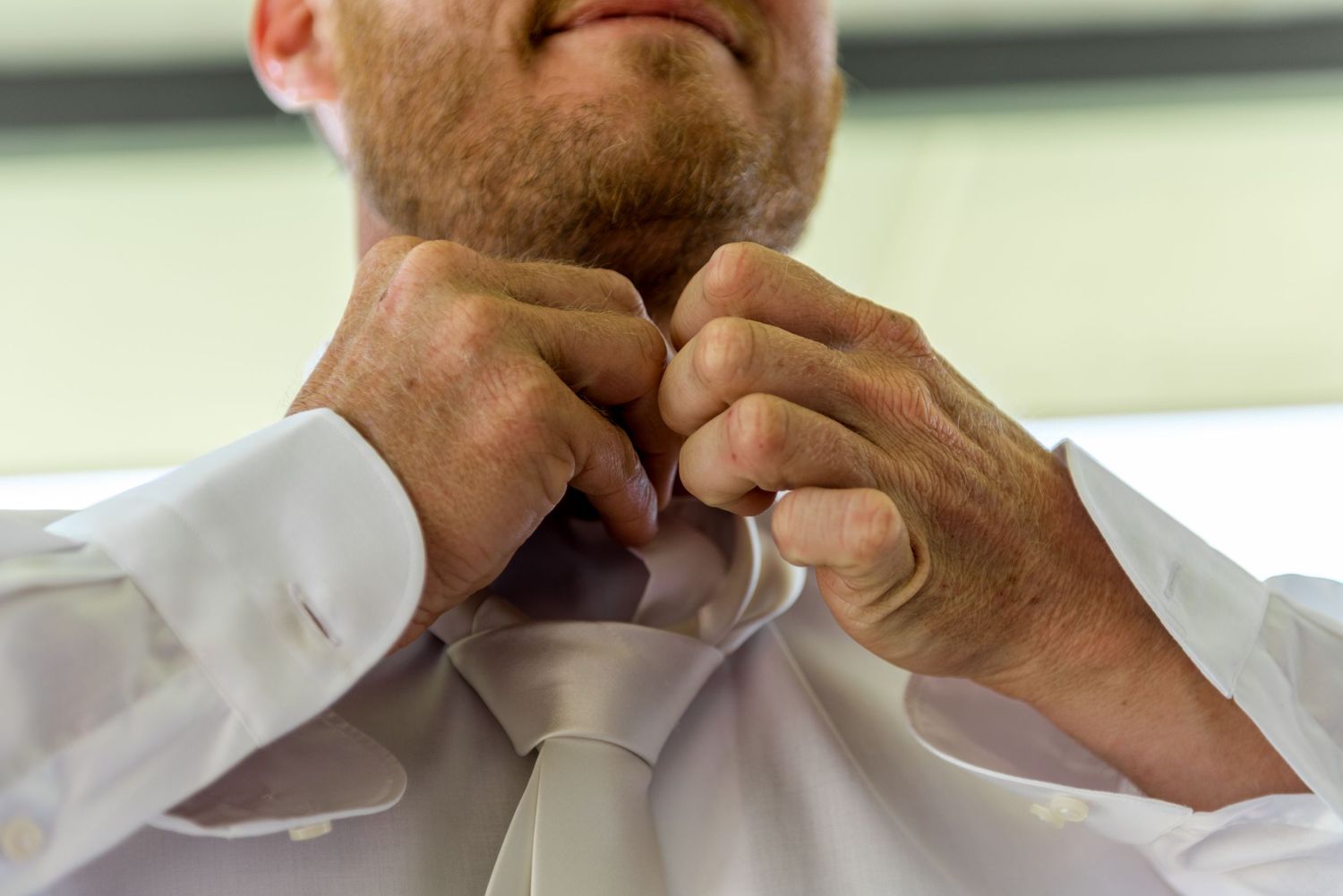 Close-up of a groom adjusting his white tie while getting dressed for his wedding day.