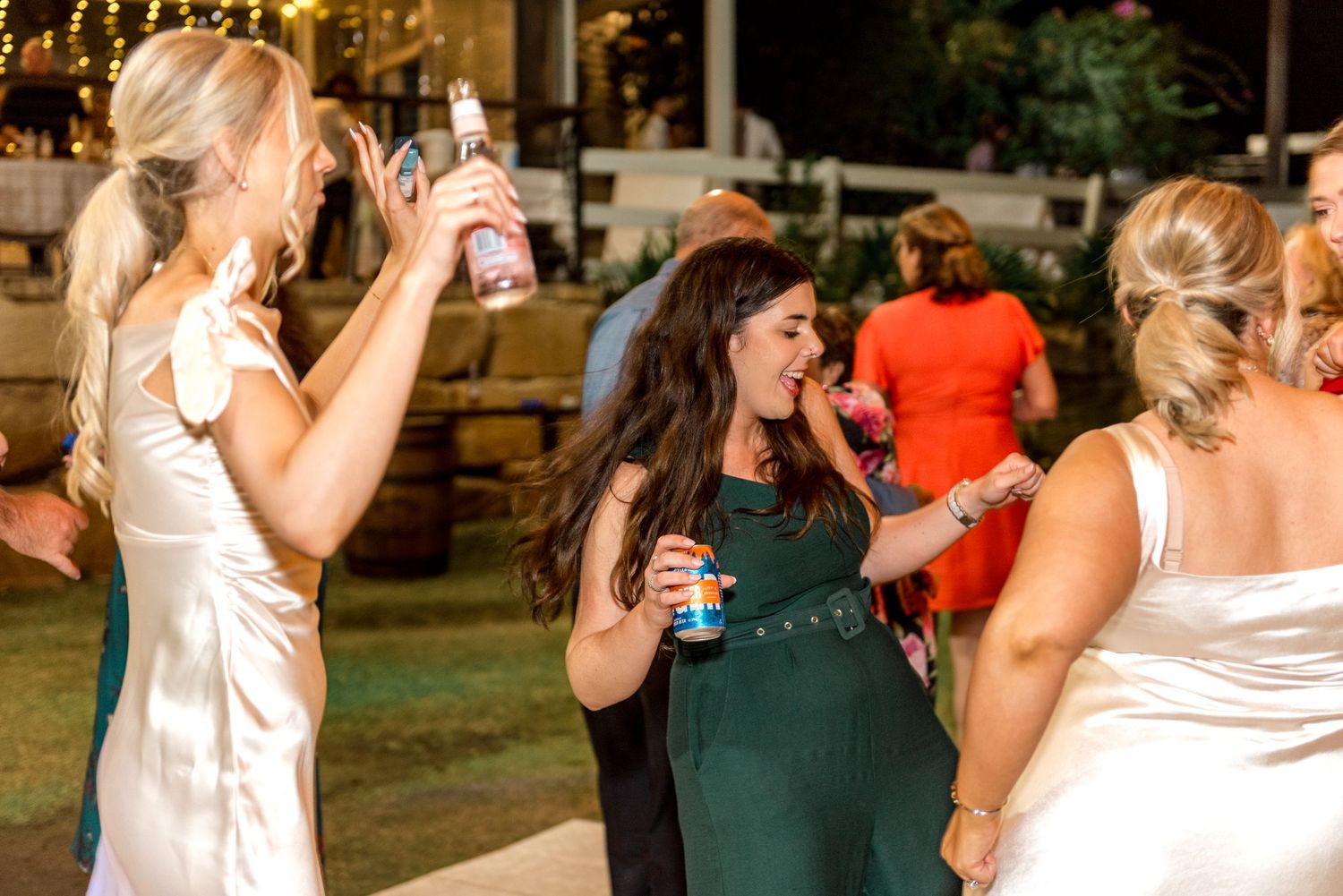 Women in elegant dresses dancing and celebrating at an outdoor wedding reception at night.