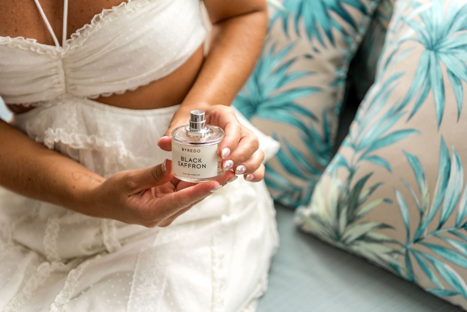 Bride holding Black Saffron perfume bottle in white wedding dress.