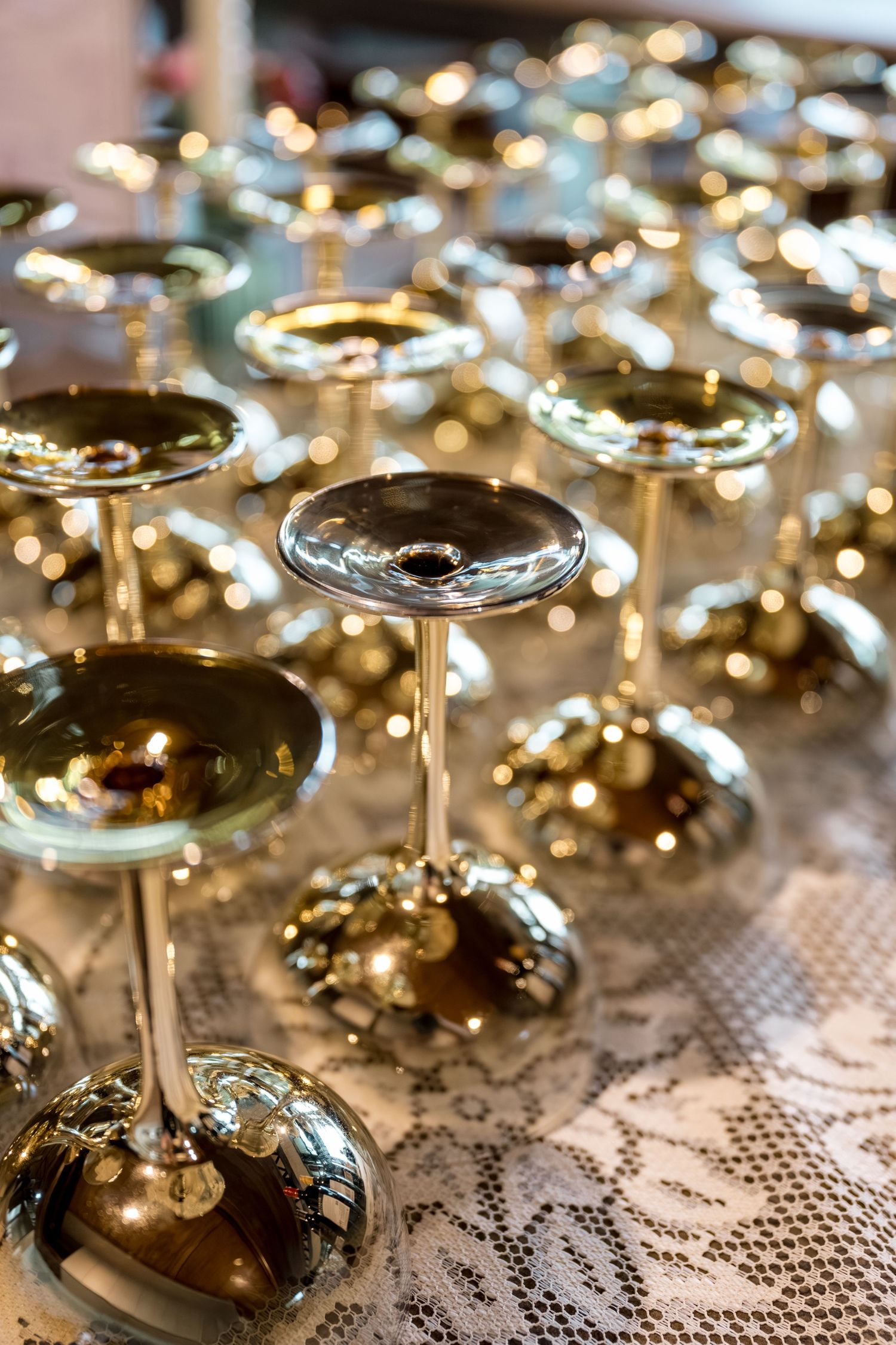 Rows of elegant upside-down gold-tinted champagne coupe glasses arranged on a lace-covered table.