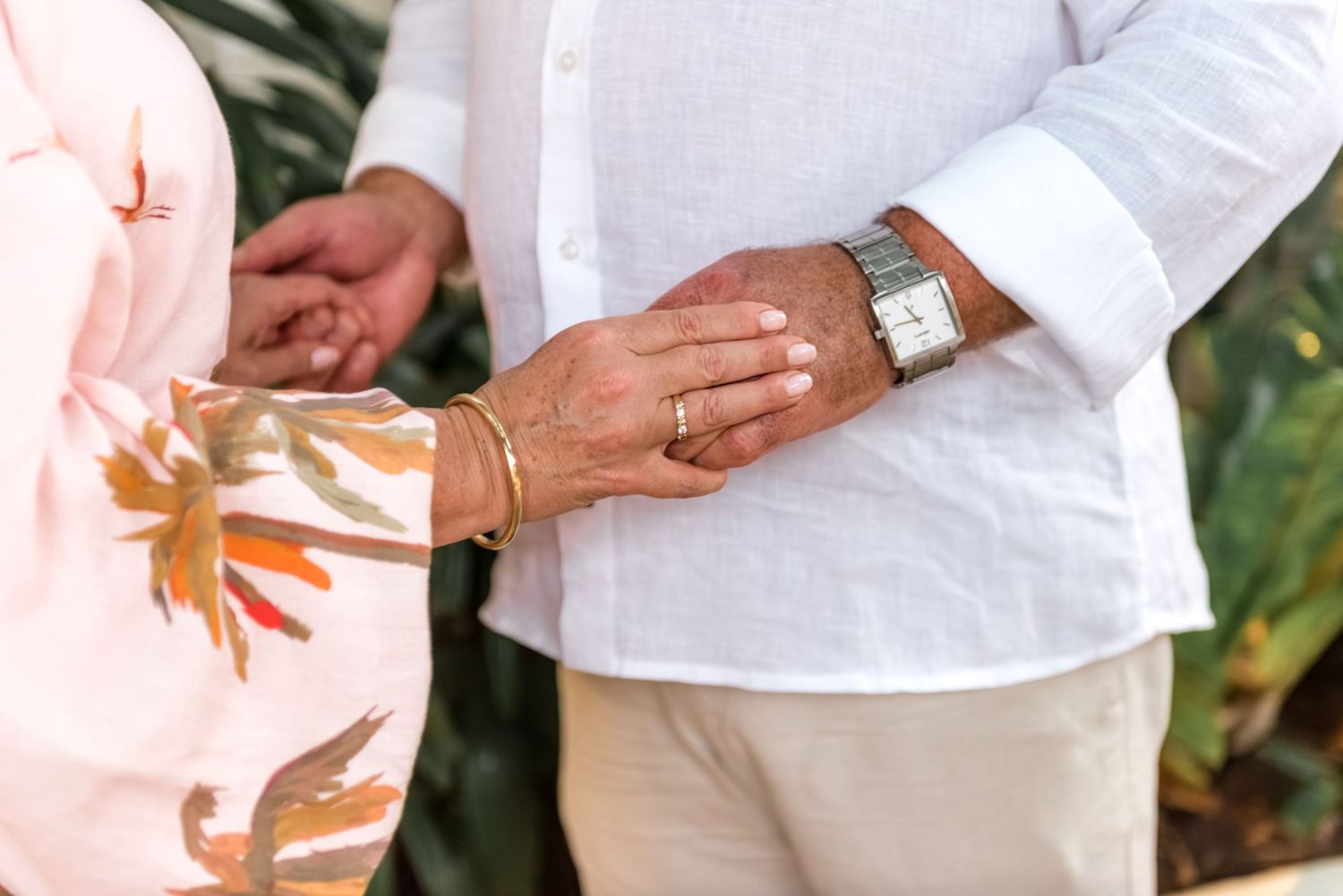 Close-up of couple holding hands showing wedding rings and gold bracelet during ceremony.