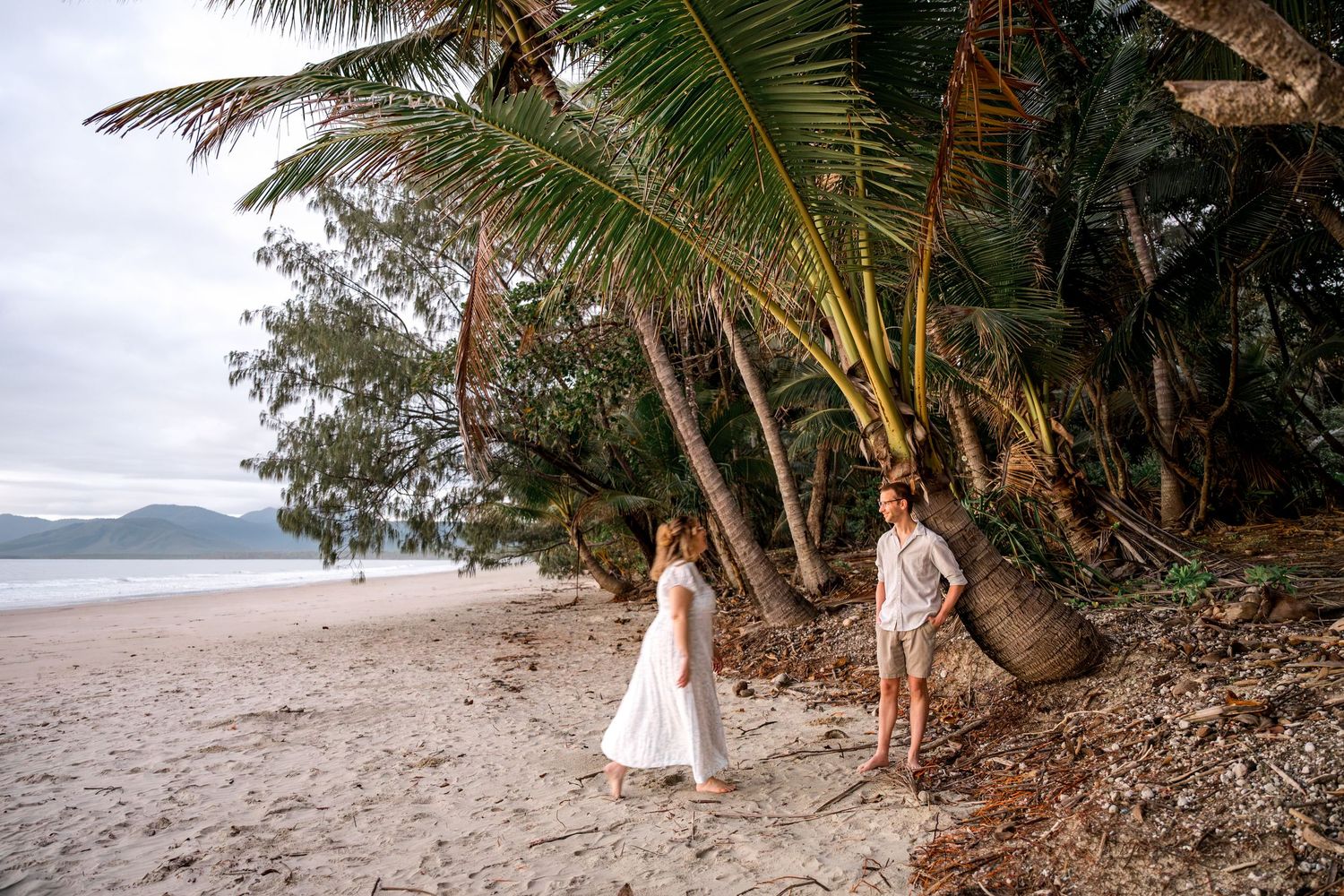 Bride and groom walking along a tropical beach lined with palm trees at sunrise at Four Mile Beach, Port Douglas.