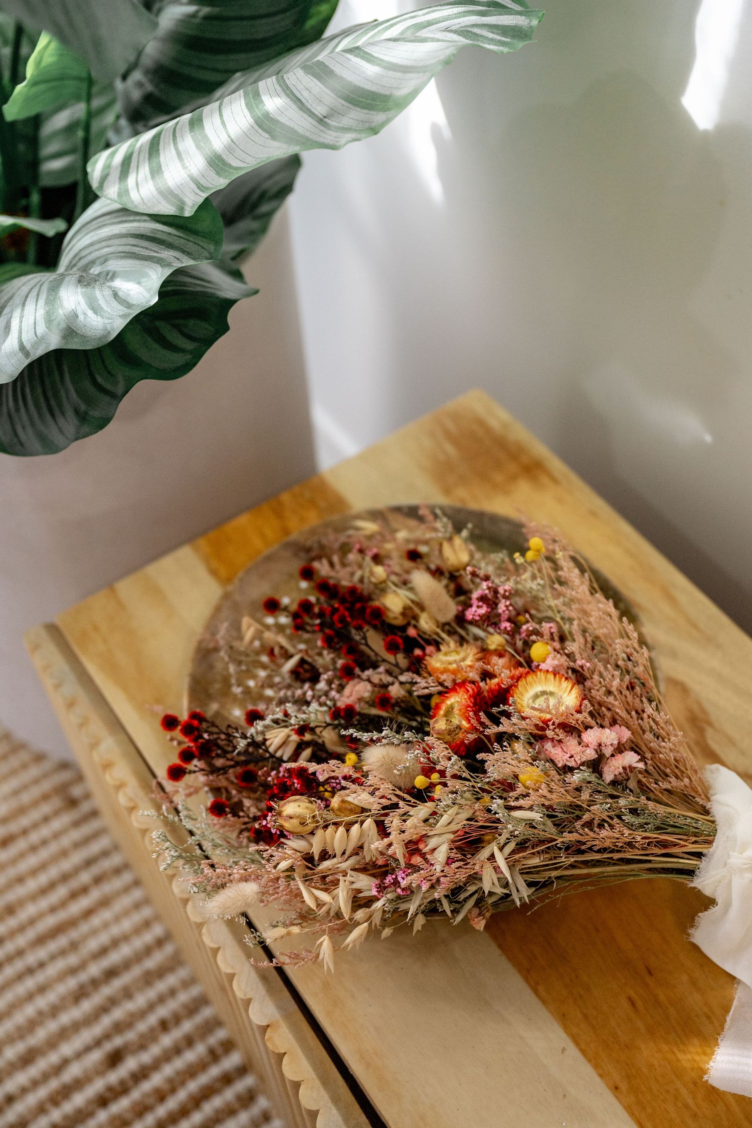 Rustic dried flower bridal bouquet with orange, pink and red blooms resting on wooden chest.