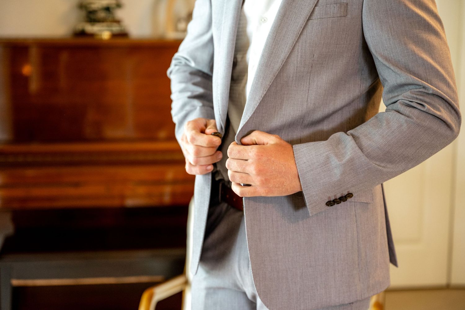 Close-up of groom in light grey suit buttoning jacket before wedding ceremony.