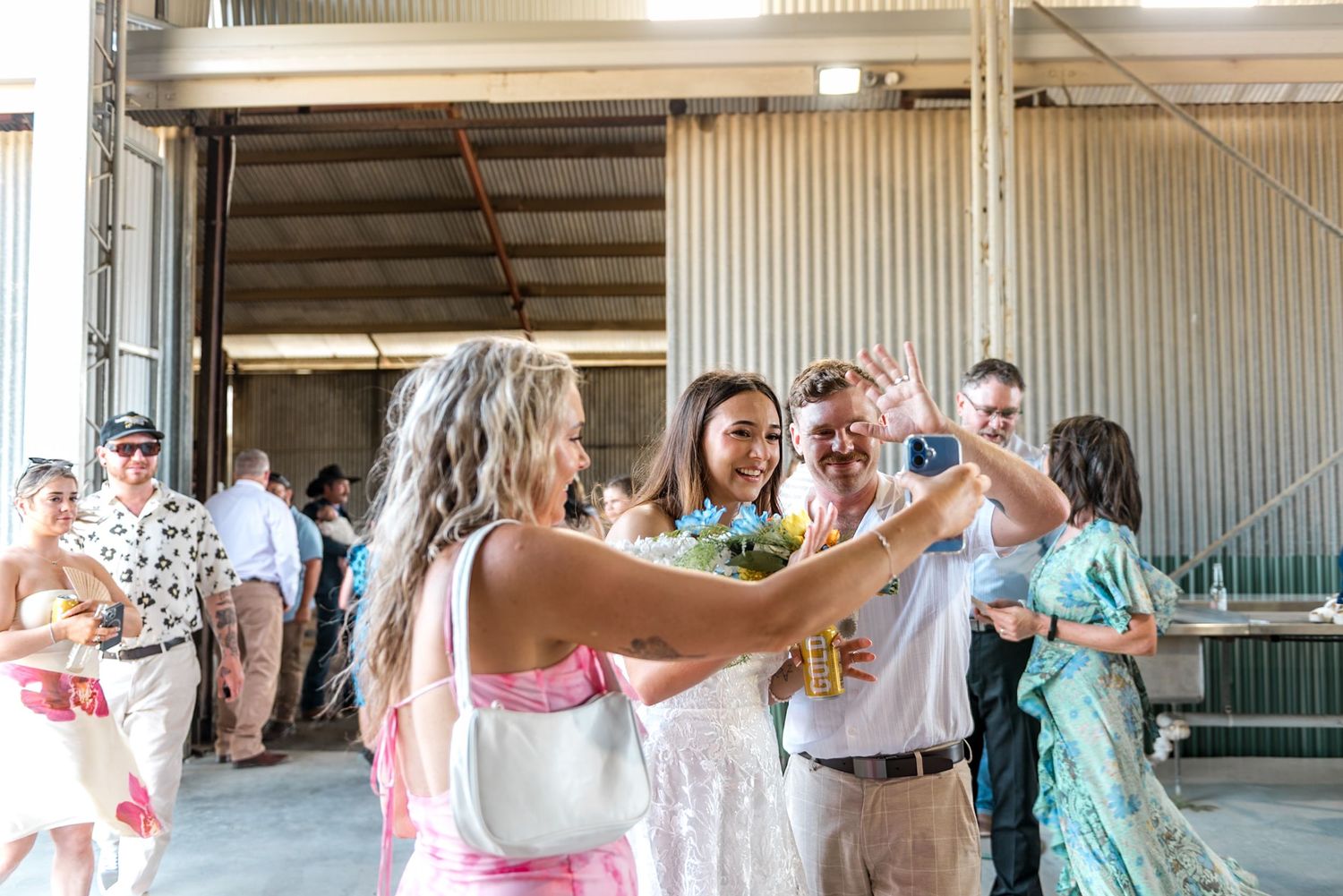 Bride in white dress dances and celebrates with guests at an outdoor barn wedding reception.