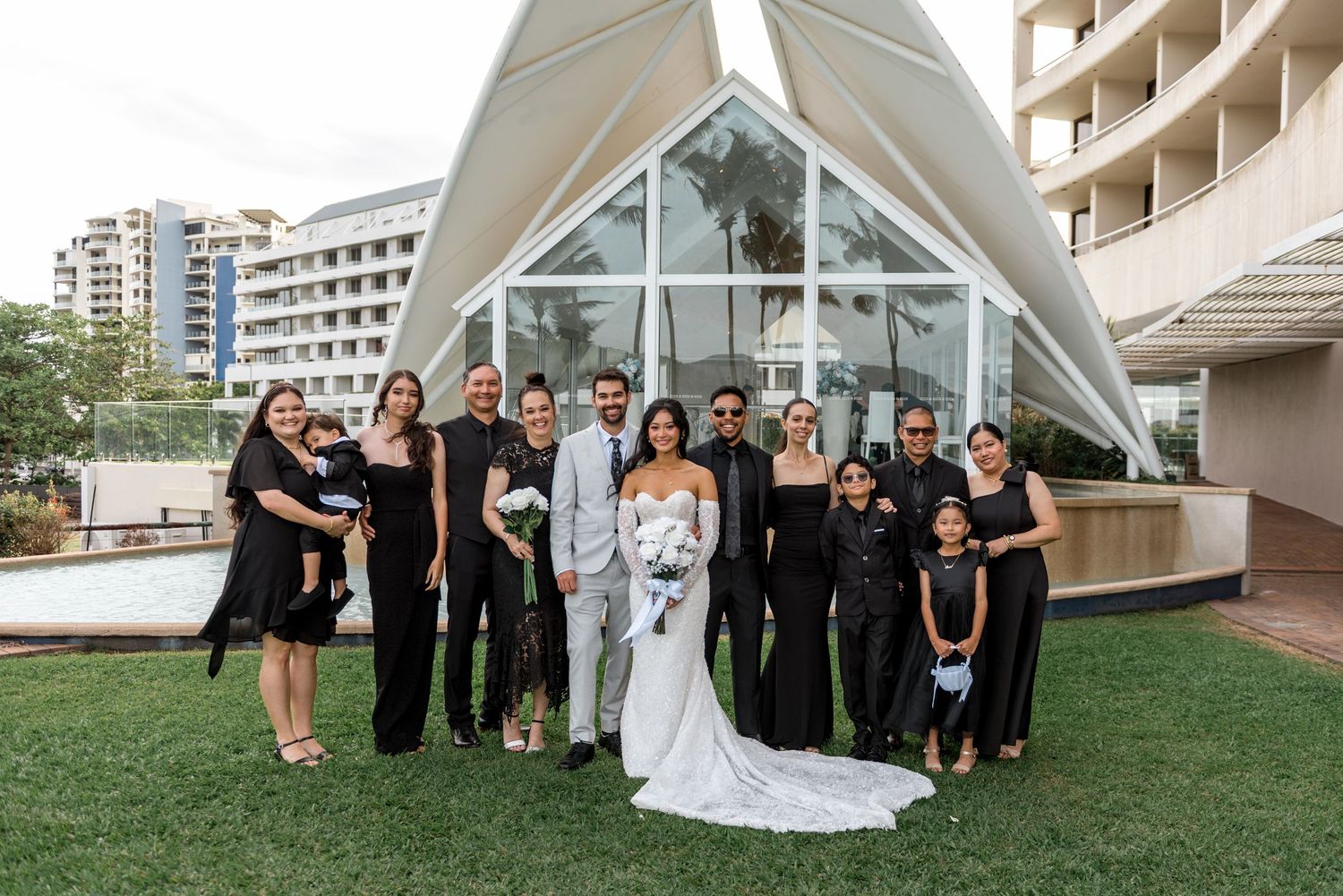 Wedding party group photo in black and white attire outside modern geometric chapel venue.