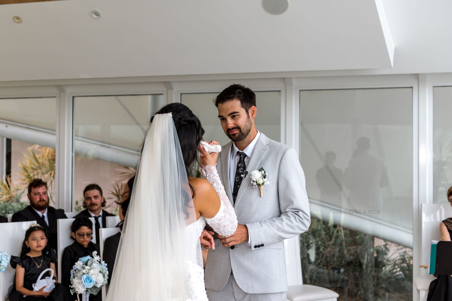 Groom in gray suit holding bride's hand during emotional wedding vow exchange at ceremony.