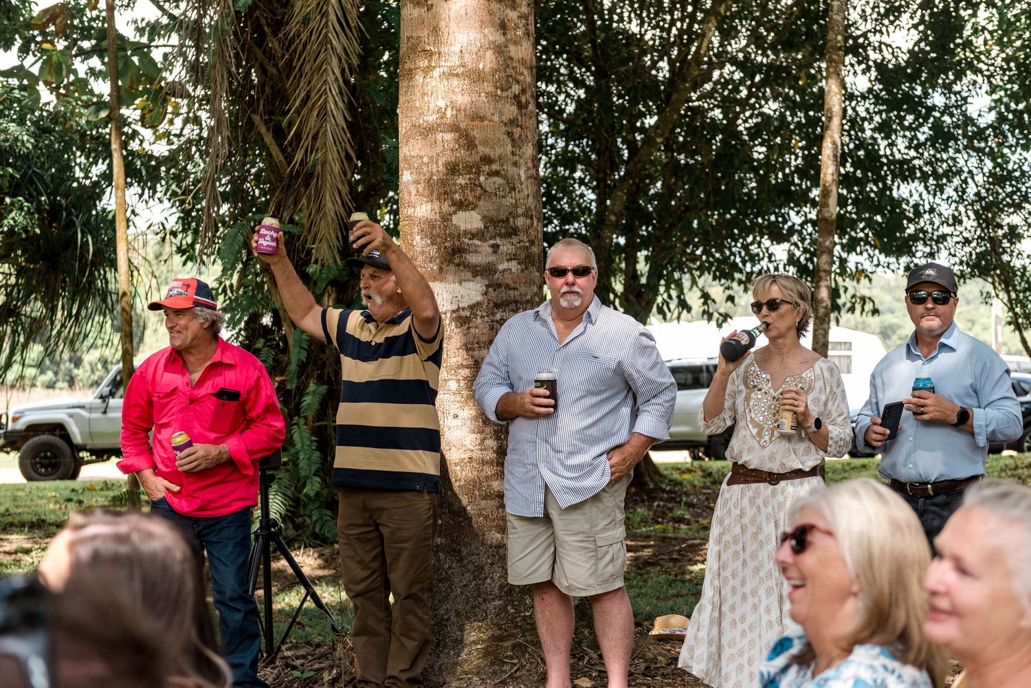 Guests socializing outdoors near trees at a casual wedding celebration in a garden setting.