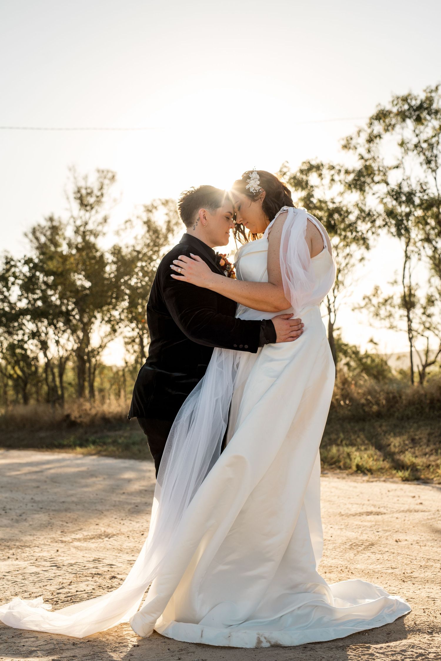 Bride and groom touching foreheads romantically at sunset on a dirt road.