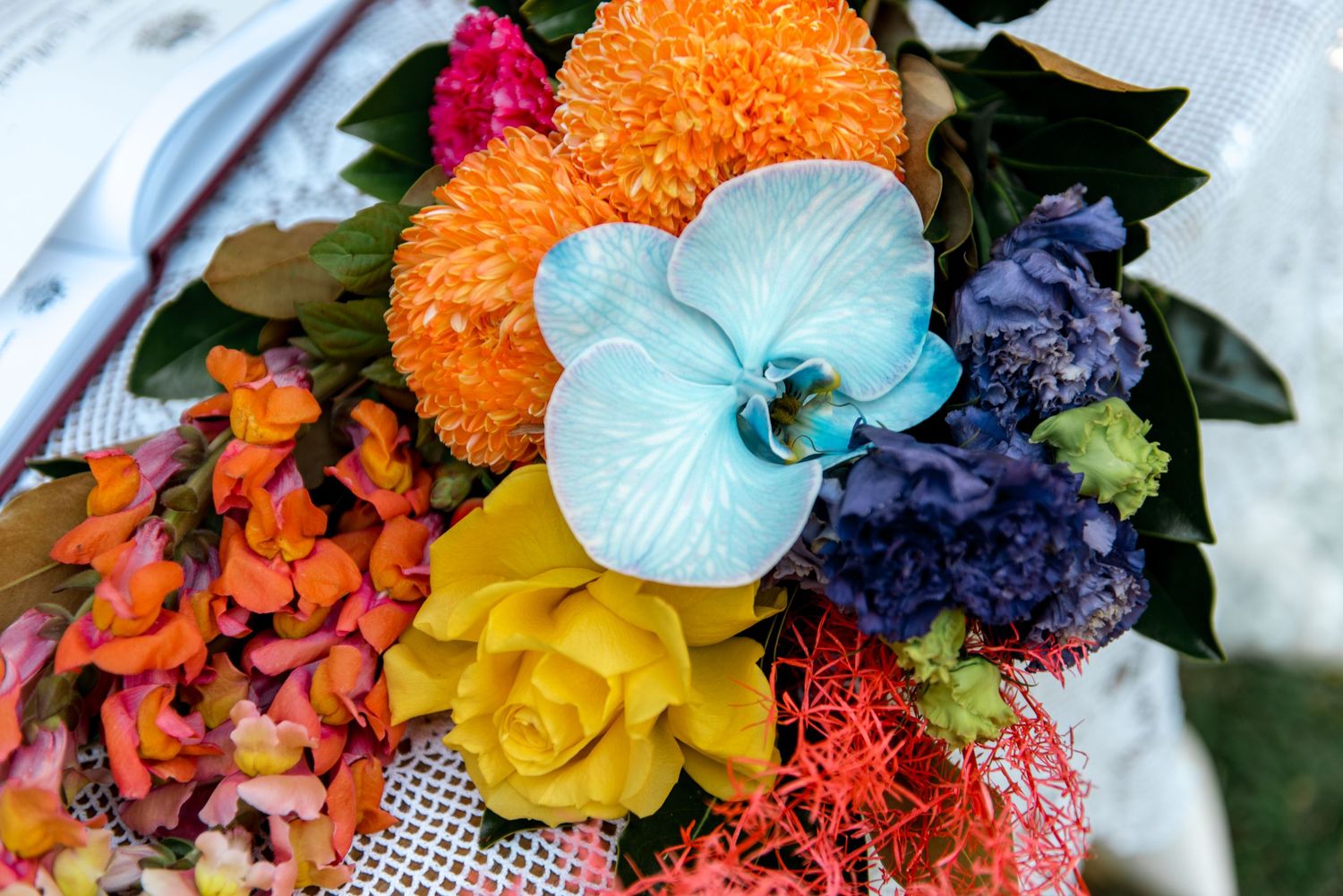 Vibrant wedding bouquet featuring blue orchid, orange chrysanthemum, yellow rose, and colorful tropical flowers.