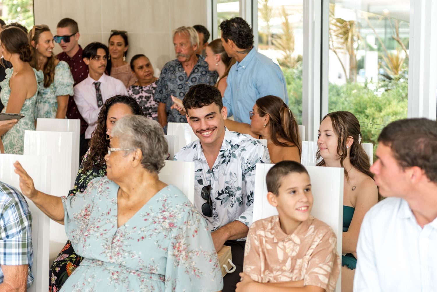 Wedding guests mingling and smiling in a bright, modern ceremony venue with white chairs.
