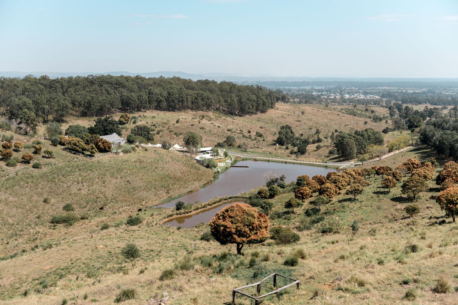 Aerial view of rural Australian countryside with winding road, dam, and sparse dry landscape.