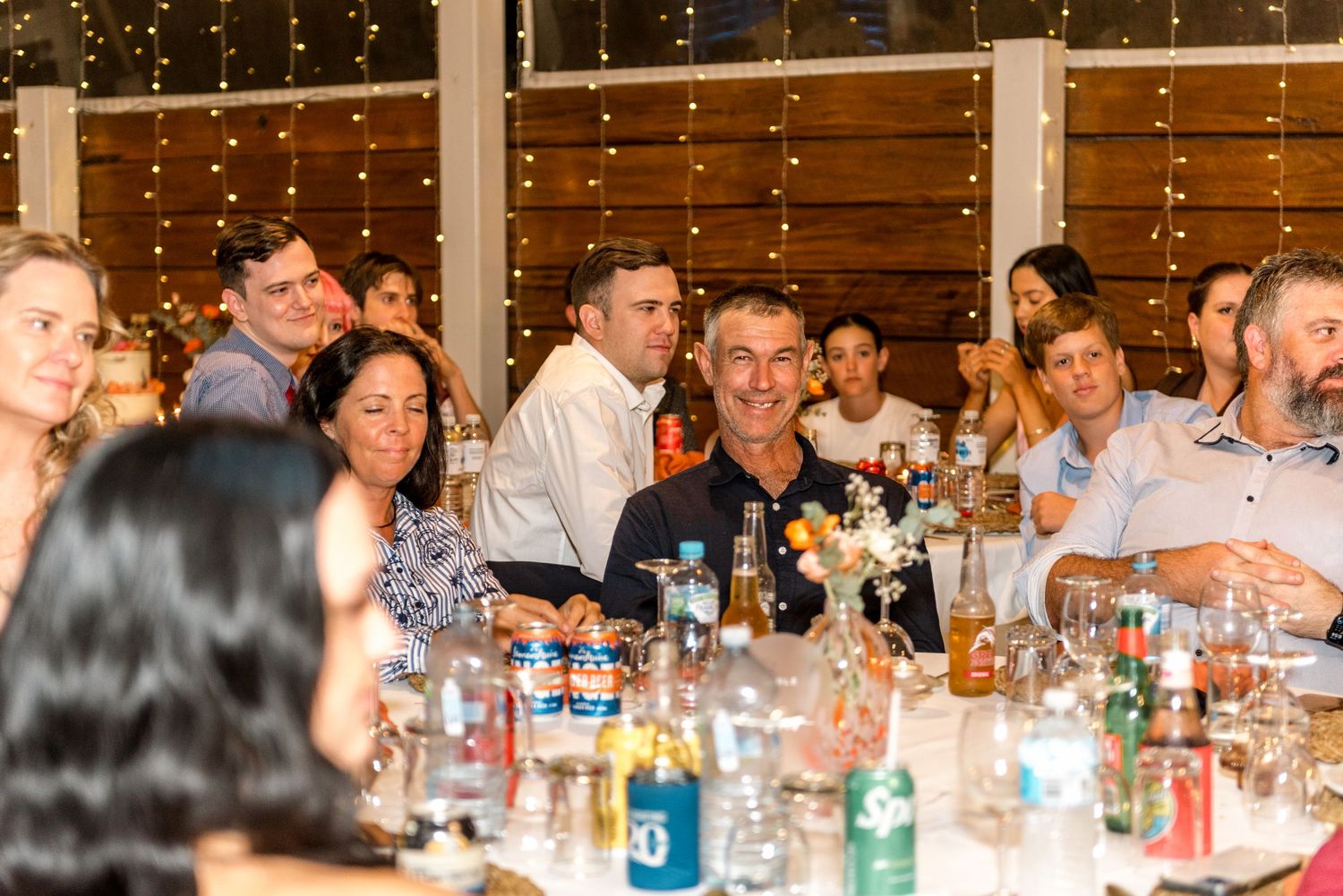 Wedding guests laughing and celebrating at decorated reception tables with fairy lights.