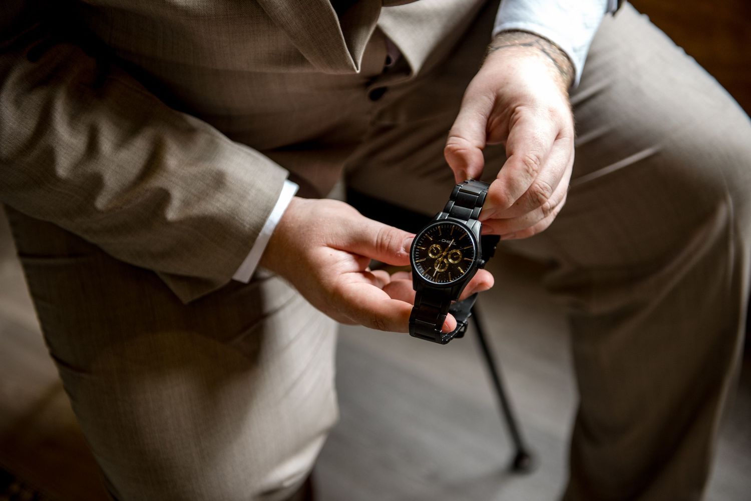 Groom adjusting elegant black and gold dress watch while wearing a beige wedding suit.