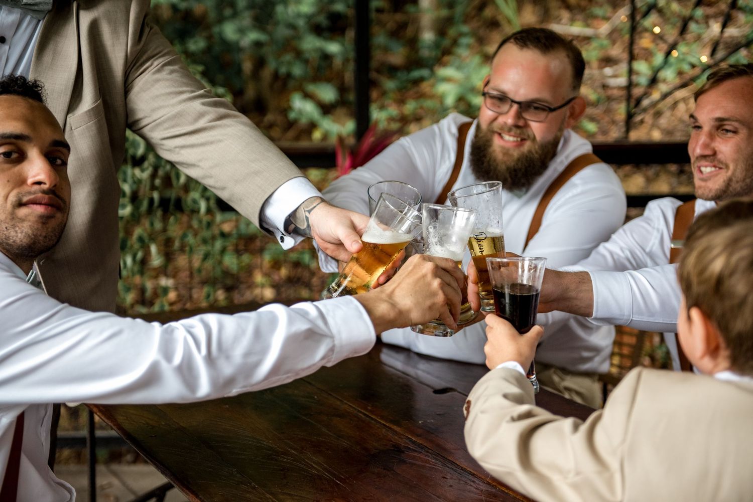 Groomsmen clinking glasses of beer and drinks together in a joyful wedding day toast.