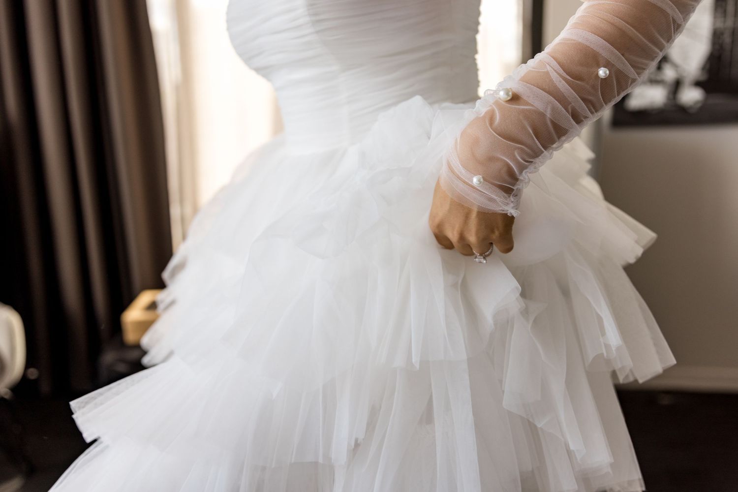Detail shot of bride in ruffled tulle wedding dress with sheer pearl-embellished long sleeve glove.