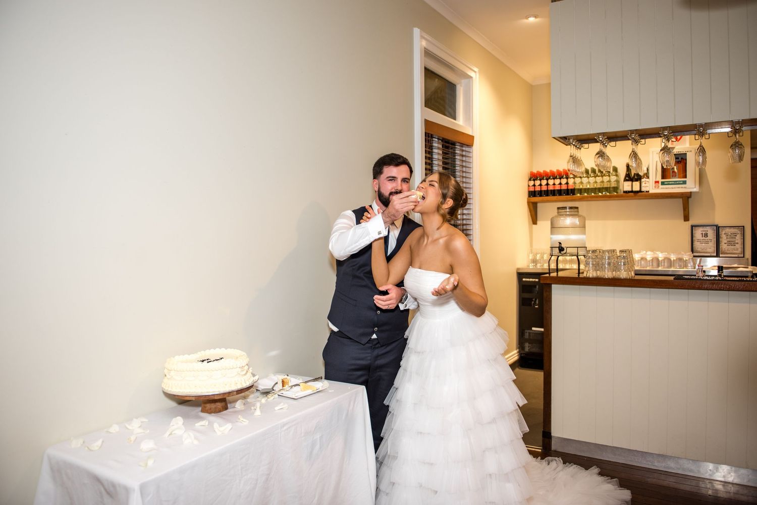 Bride and groom sharing a romantic kiss beside their wedding cake at their reception.