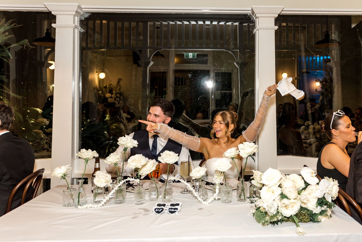 Bride and groom raising napkins in celebration at their wedding reception sweetheart table.