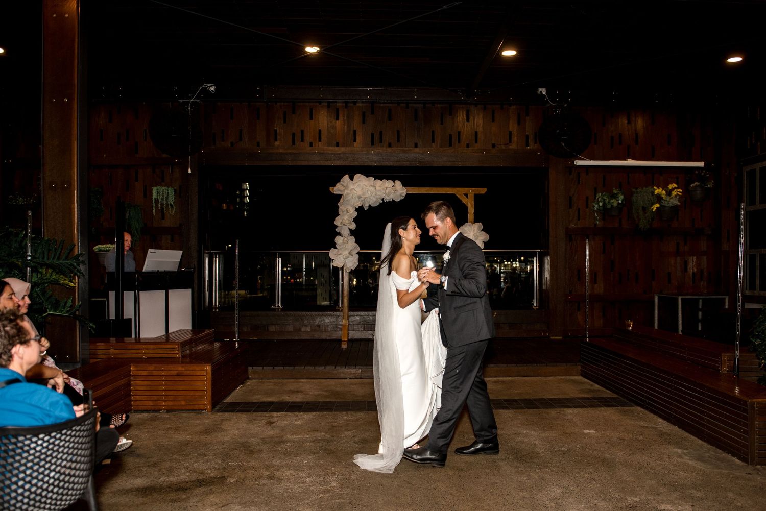 Bride in white gown and groom in dark suit share a romantic first dance at their evening wedding reception.