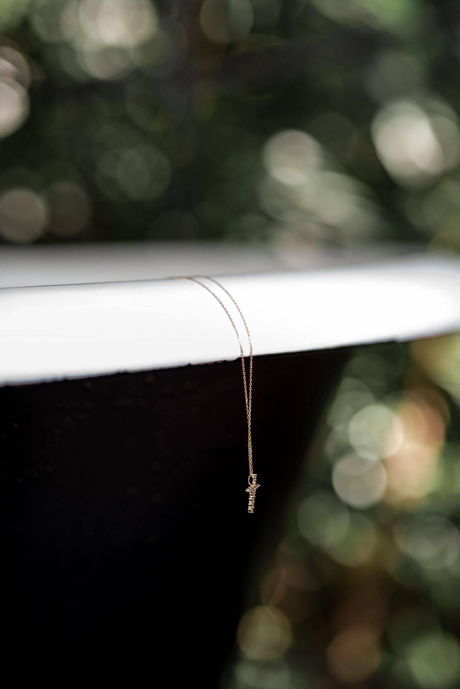 Delicate gold cross necklace on a thin chain displayed against a blurred green bokeh background.