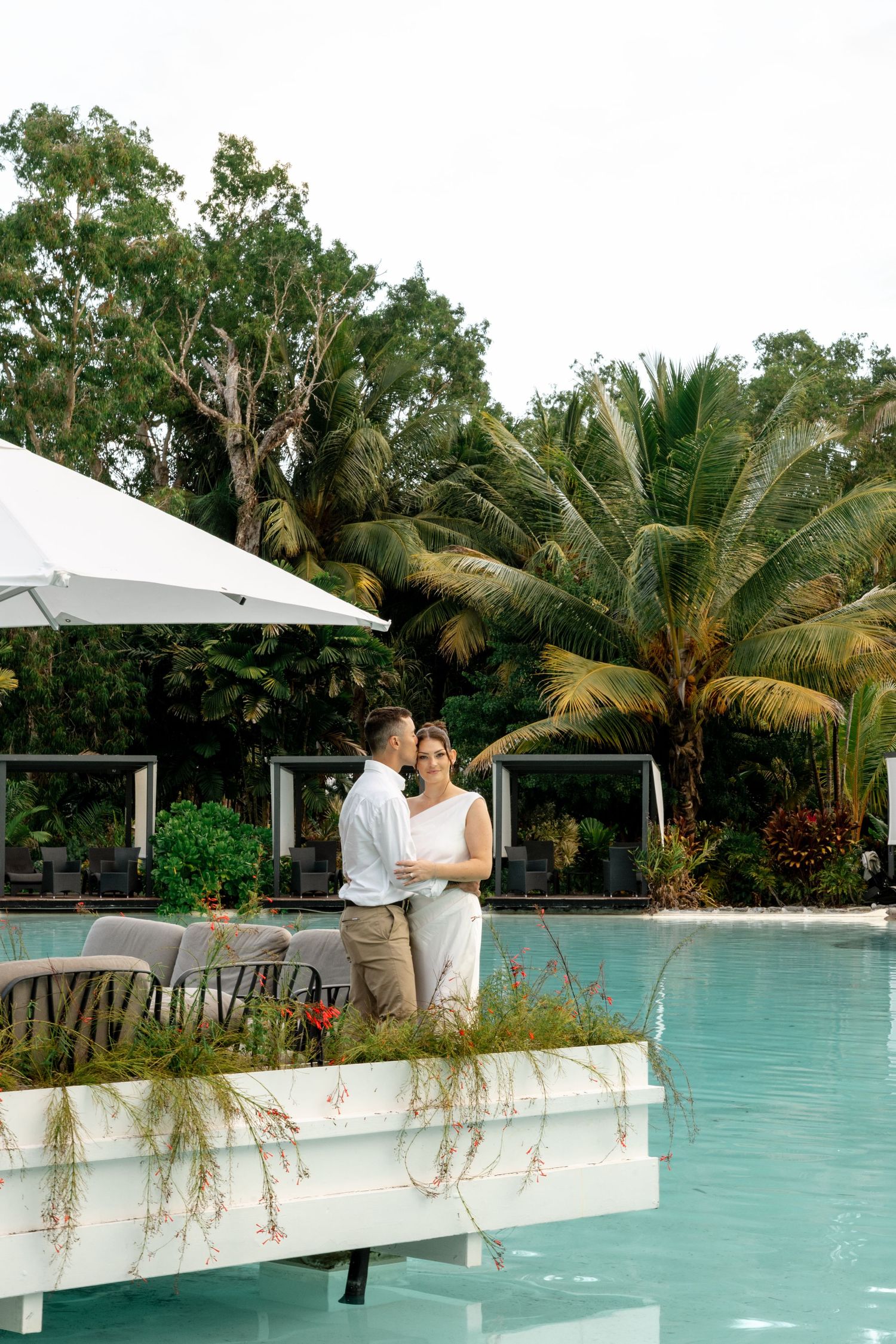 Elegant couple standing together by a luxury tropical resort pool with lush palm trees at Sheraton Grand Mirage Port Douglas.