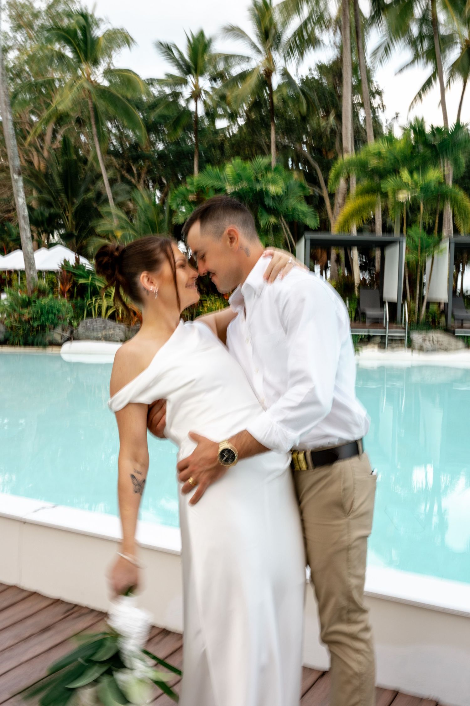 Bride and groom sharing a romantic kiss poolside at a lush tropical resort surrounded by palm trees at Sheraton Grand Mirage Port Douglas.