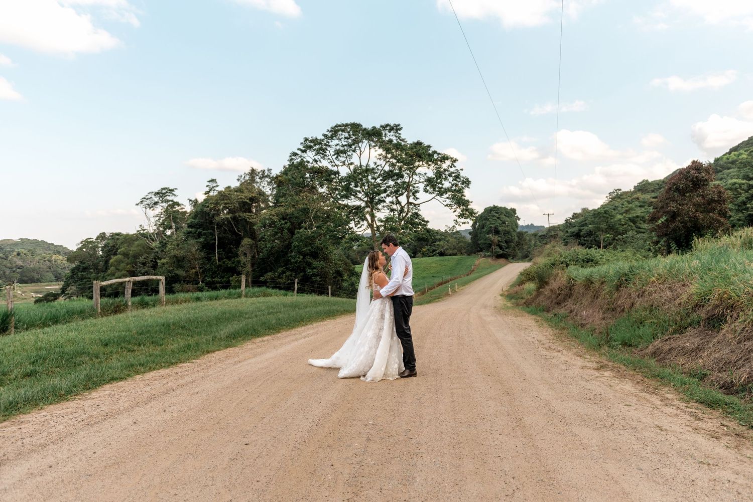 Wedding couple sharing a romantic moment on a peaceful countryside dirt road with green hills.