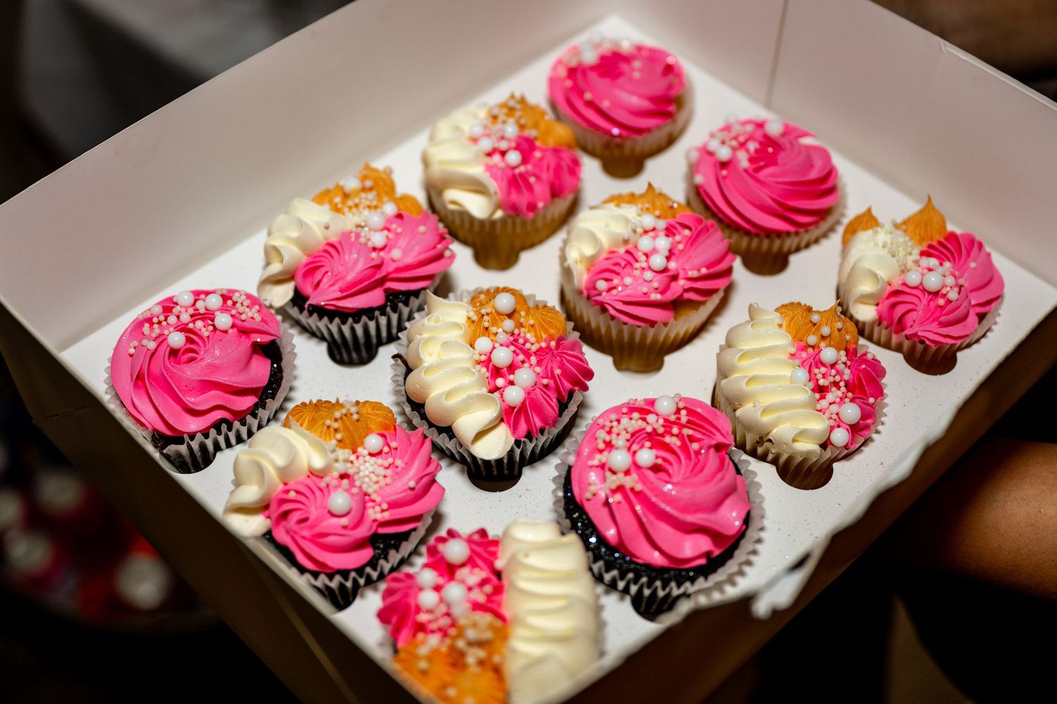 Box of elegant pink and white frosted cupcakes with pearl decorations.