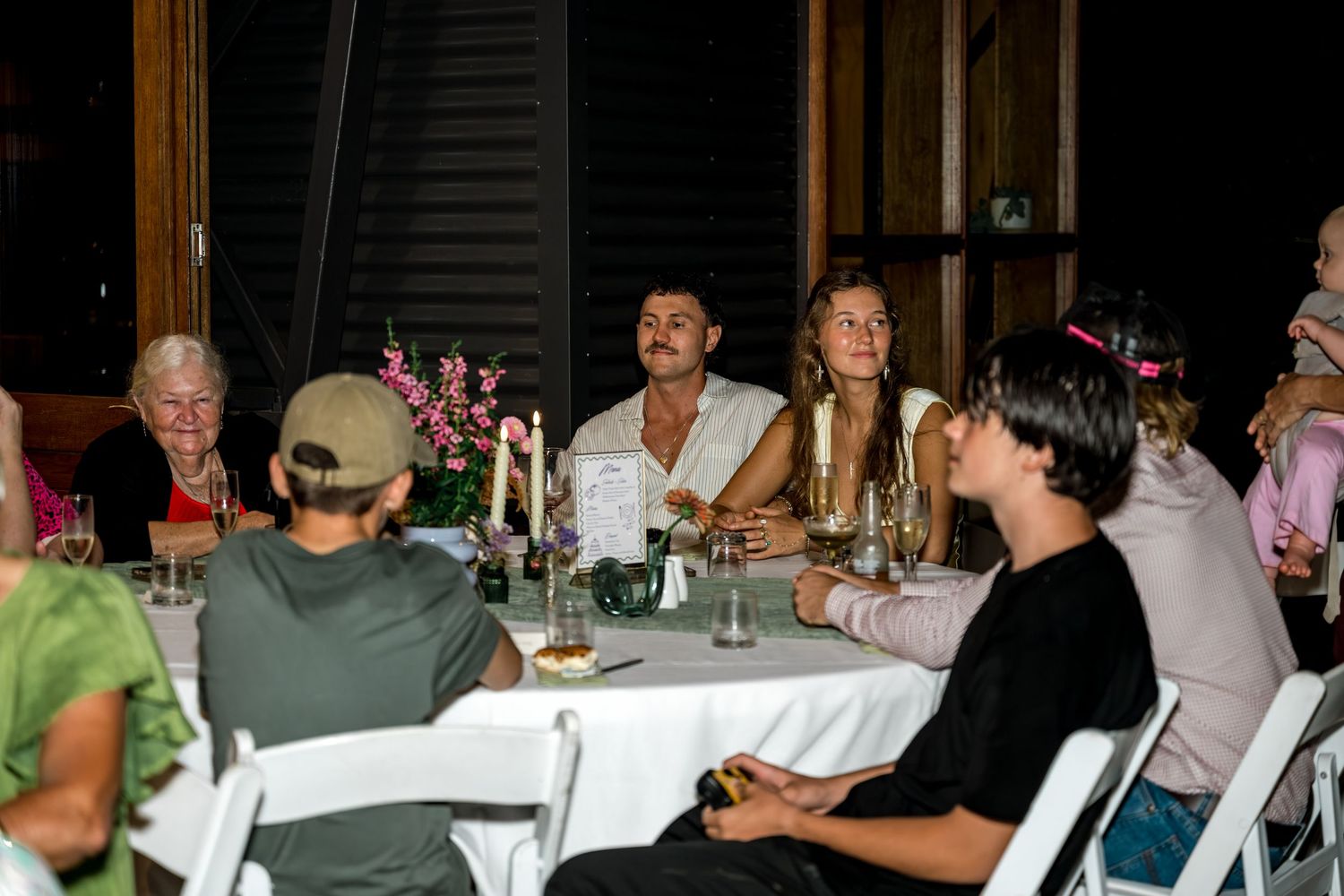Wedding guests seated at a round table with candles and floral centerpieces during dinner.