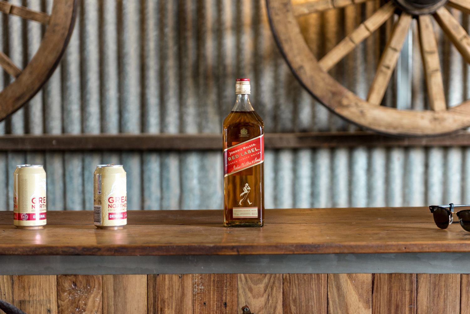 Johnnie Walker Red Label whisky bottle on rustic wooden bar with wagon wheels backdrop.