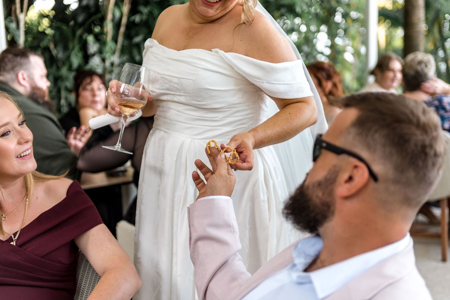 Bride in white gown holds champagne while groom in pink suit holds her hand.