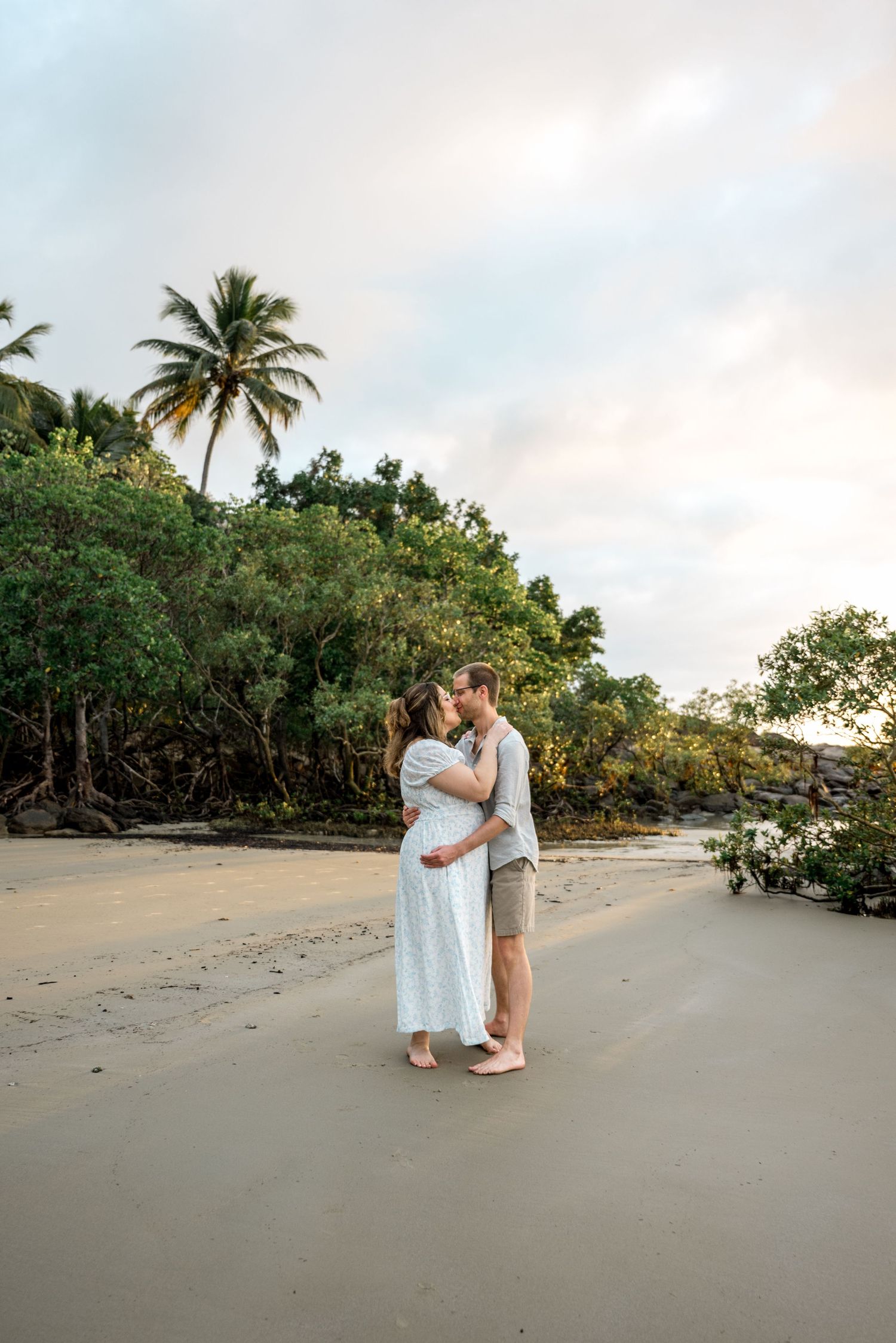 Couple sharing a romantic kiss on sandy tropical beach with palm trees at sunset at Four Mile Beach, Port Douglas.
